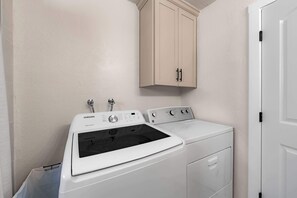 A laundry room with a front-loading washer and dryer, a cabinet above the dryer, and a door to the right. - Tree Top Verdon 5BDR with Sauna (South Lake Tahoe)