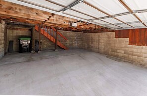 A basement with a concrete floor, wooden walls, a metal staircase, and a garage door. - Tree Top Verdon 5BDR with Sauna (South Lake Tahoe)