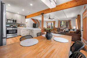 A modern kitchen with stainless steel appliances, a dining area with a wooden table and chairs, and a living room with a sofa and a television. - Tree Top Verdon 5BDR with Sauna (South Lake Tahoe)