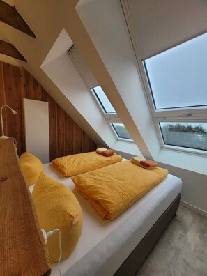 A modern bedroom with a sloped ceiling, skylights, and a bed with yellow bedding. - Apartment 3 in the Flechtner Building (Norderney)