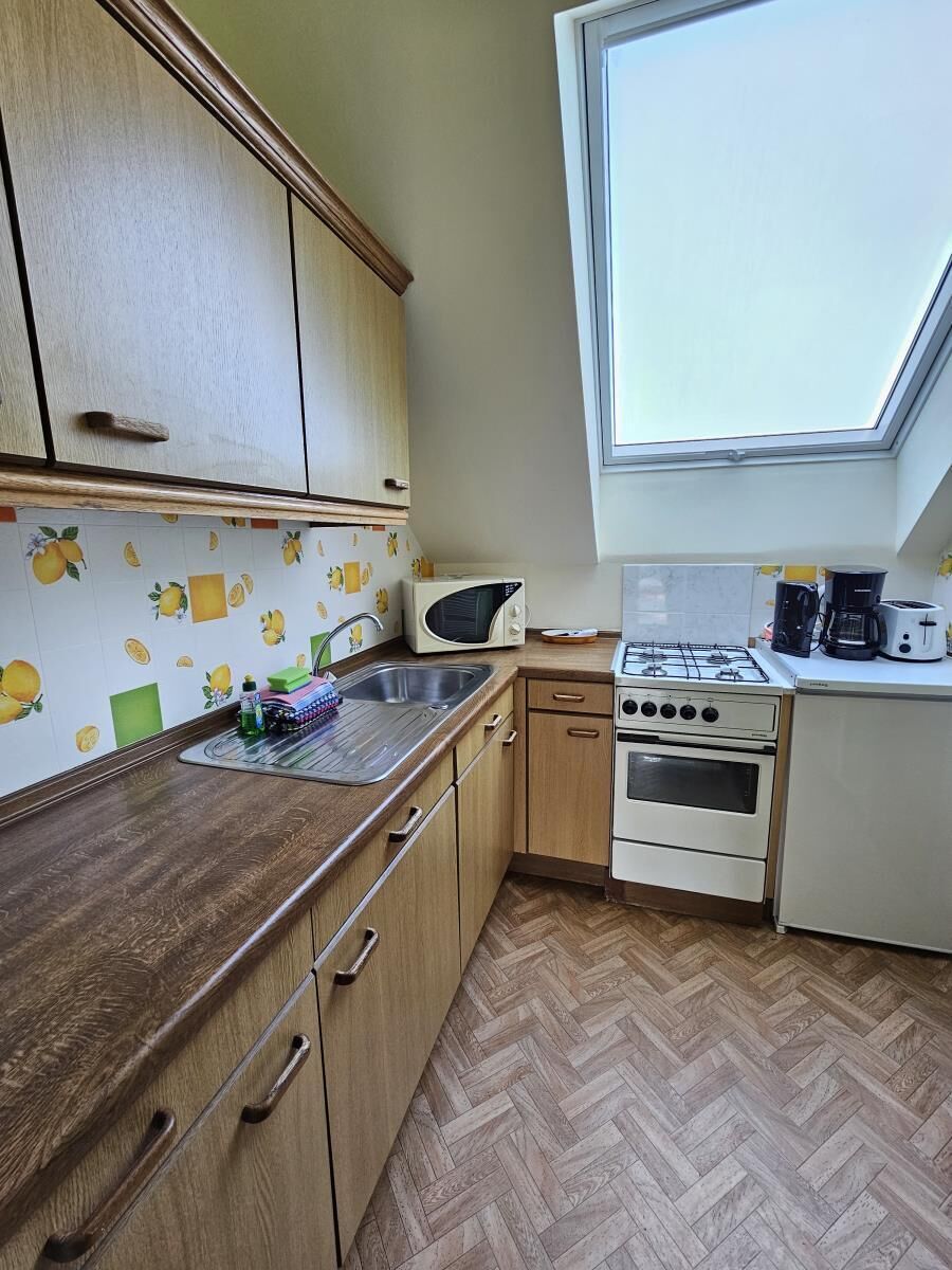 A compact kitchen with a herringbone floor pattern, a gas stove, a microwave, and a sink.