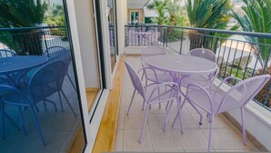 A balcony with outdoor seating, including round tables and chairs, and a view of a garden with palm trees. - 09 Relais du Lac Charme - Italian Homing (Desenzano del Garda)