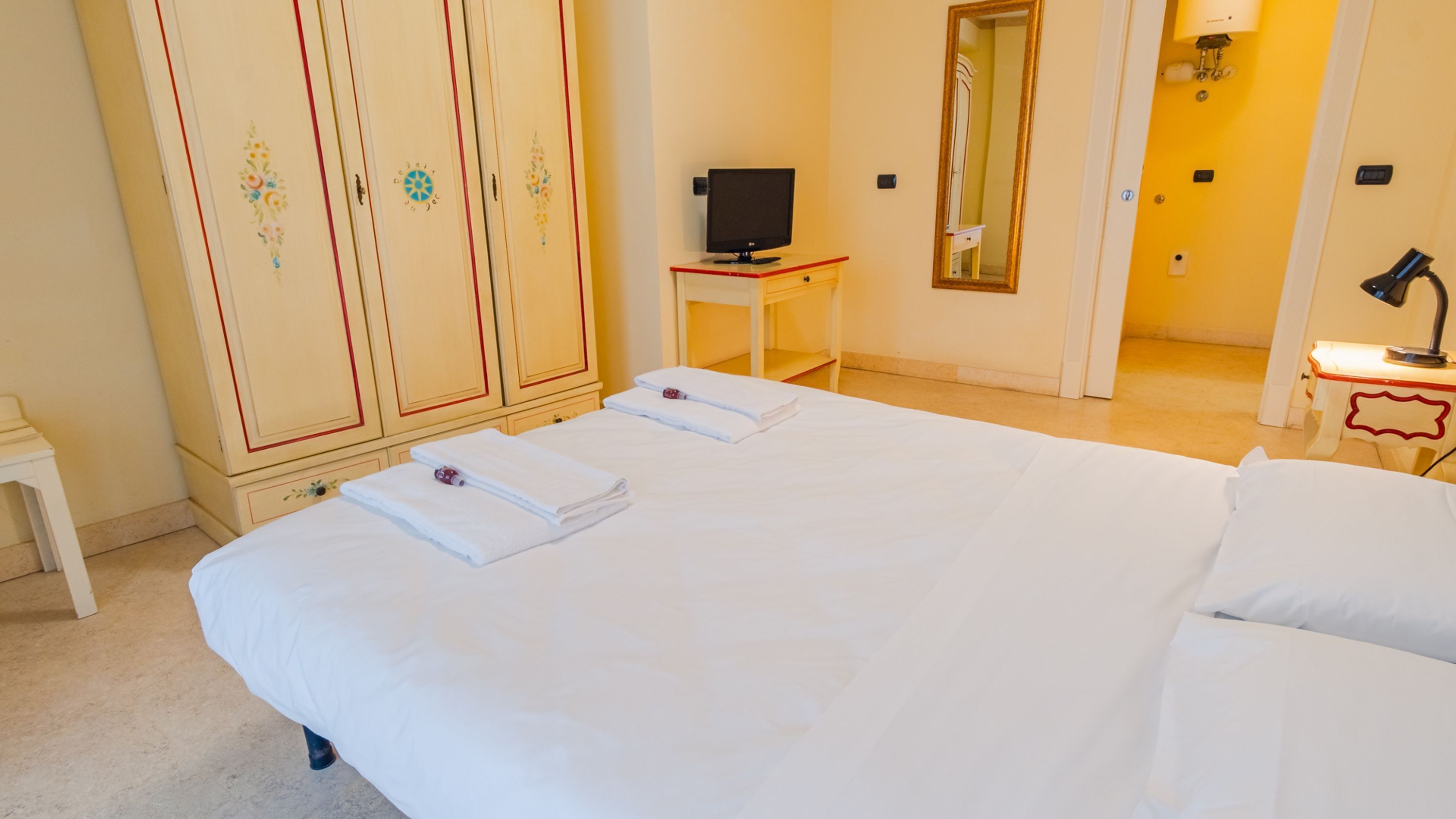 A hotel room with a large bed, a television, a mirror, and a small table with a lamp.