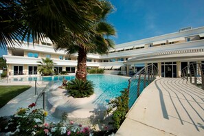 Ein Poolbereich mit einer Palme, ein Gebäude mit mehreren Balkonen und einem überdachten Gang.