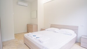 A clean, minimalist bedroom with a wooden bed, a nightstand, a small wooden dresser, and a wall-mounted air conditioner. - 20 Relais du Lac Elite - Italian Homing (Desenzano del Garda)
