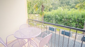 Ein Balkon mit rundem Tisch und vier Stühlen, der auf einen üppigen Garten mit verschiedenen Pflanzen und einer Palme blickt.