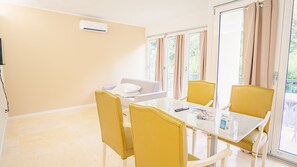 A hotel room with a dining table, yellow chairs, a white sofa, and a sliding glass door to the outside. - 20 Relais du Lac Elite - Italian Homing (Desenzano del Garda)