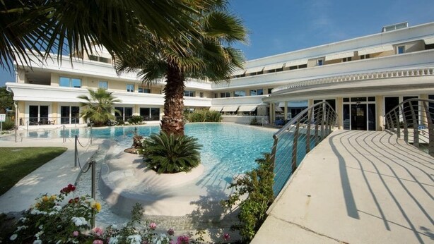 A hotel with a swimming pool, palm trees, and a covered walkway. - 20 Relais du Lac Elite - Italian Homing (Desenzano del Garda)