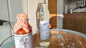 Eine Küchenzeile mit einer Gerolsteiner-Flasche, einem Marmeladenglas und leeren Weingläsern auf einem Tisch.