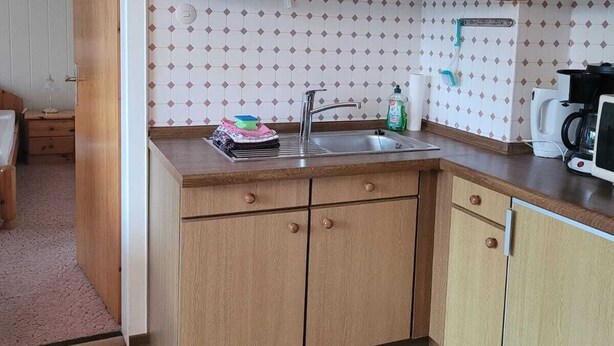 Eine kleine Küche mit Holzausstattung, einem Spülbecken und einer Kaffeemaschine.