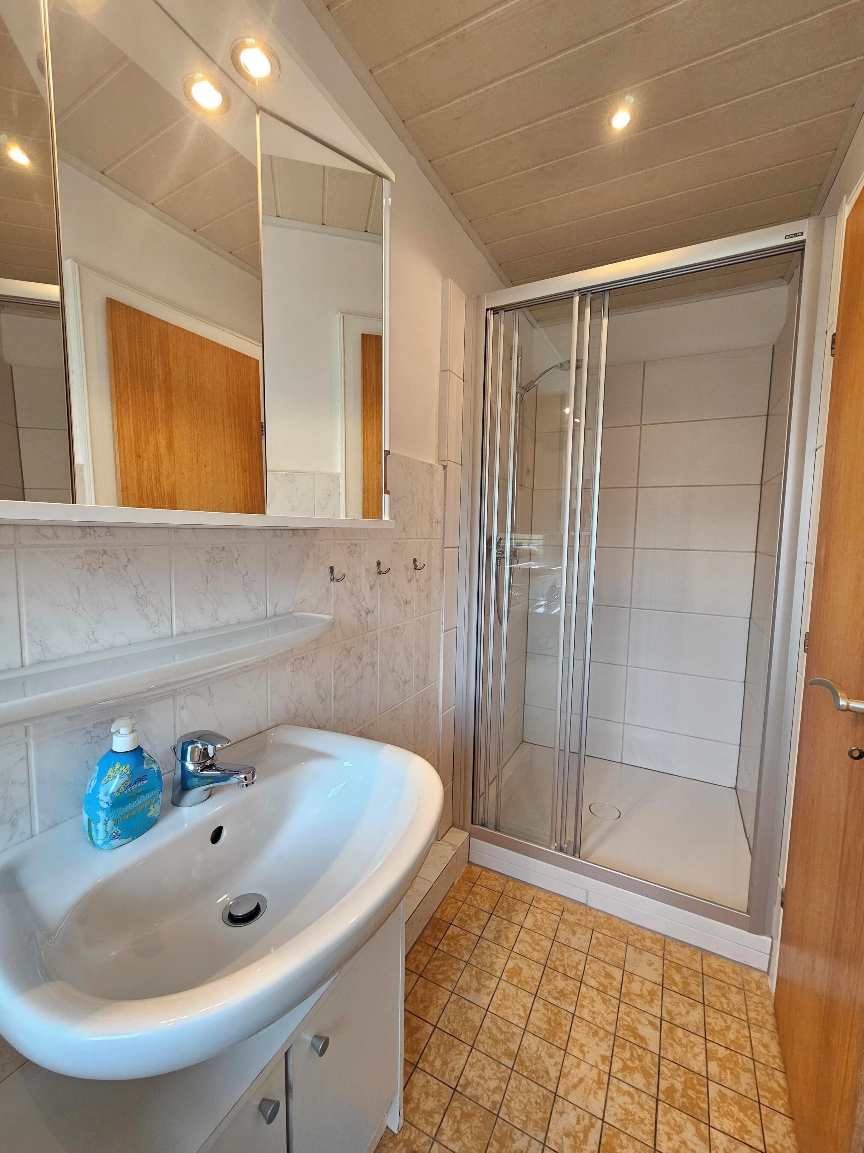 A bathroom with a white sink, a mirror, a shower enclosure, and a wooden door.
