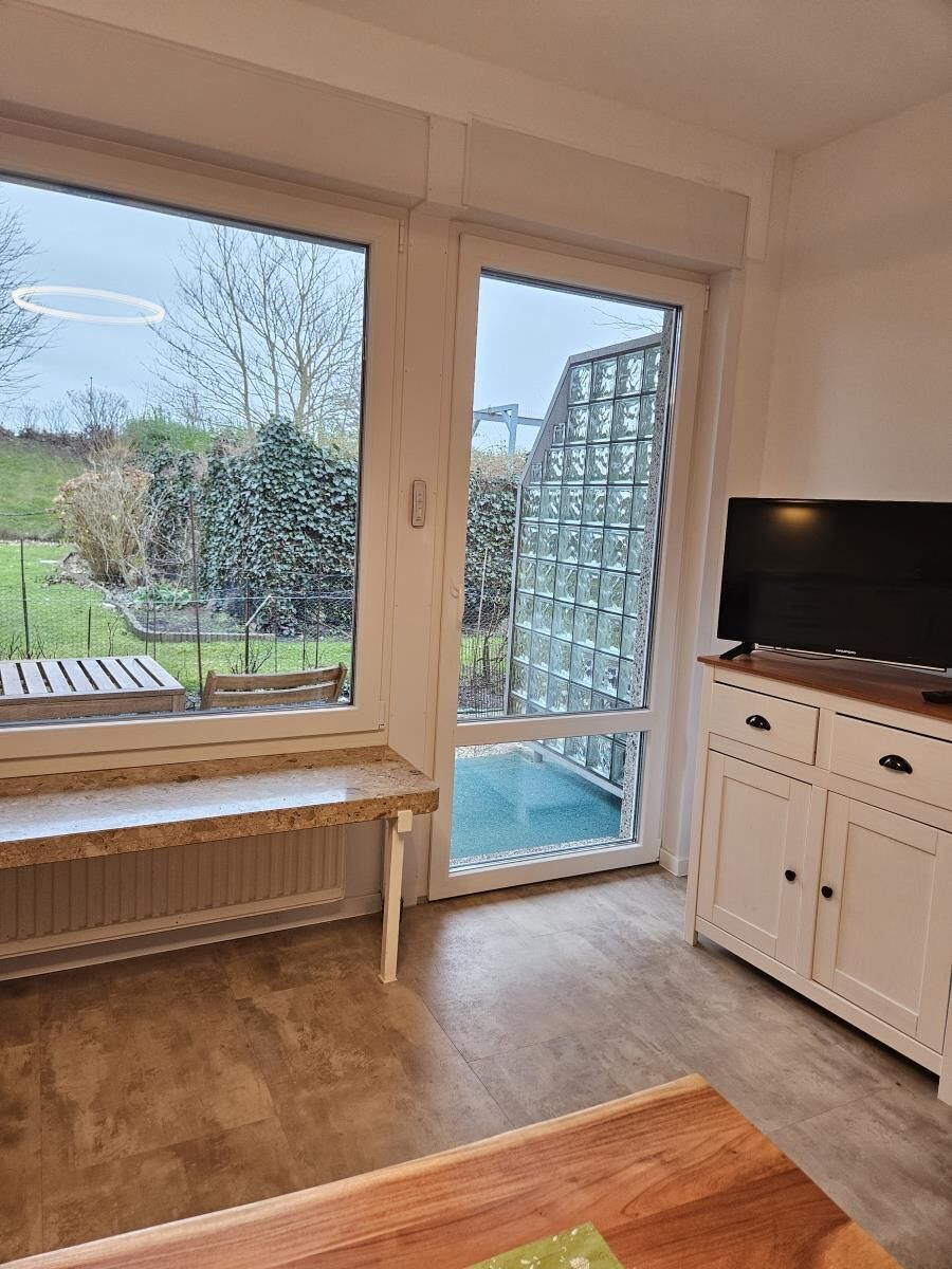 Ein Zimmer mit großem Fenster, einer Bank, einem Fernseher und einem Schrank.