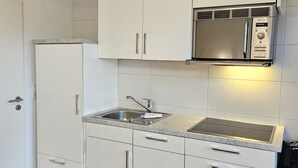 Cocina compacta con muebles blancos, un lavamanos de acero inoxidable y un microondas integrado.
