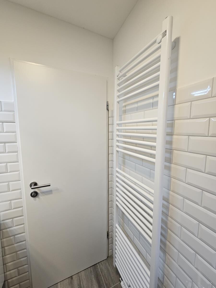 Ein Badezimmer mit weißer Tür, gefliesten Wänden in Weiß und einem weißen Handtuchhalter.