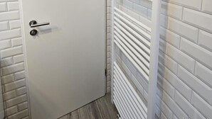 Un baño con puerta blanca, paredes cubiertas de azulejos blancos y un perchero blanco.
