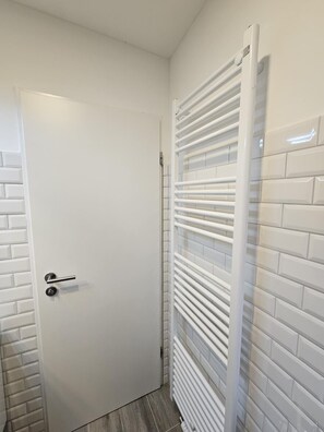 Ein Badezimmer mit weißer Tür, gefliesten Wänden in Weiß und einem weißen Handtuchhalter.
