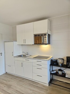 A compact kitchen with white cabinets, a built-in microwave, and a coffee maker on a black countertop. - Apartment 4 in the Flechtner Building (Norderney)
