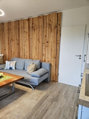 Ein modernes Wohnzimmer mit grauem Sofa, Wandverkleidung aus Holz und einem Holztisch.