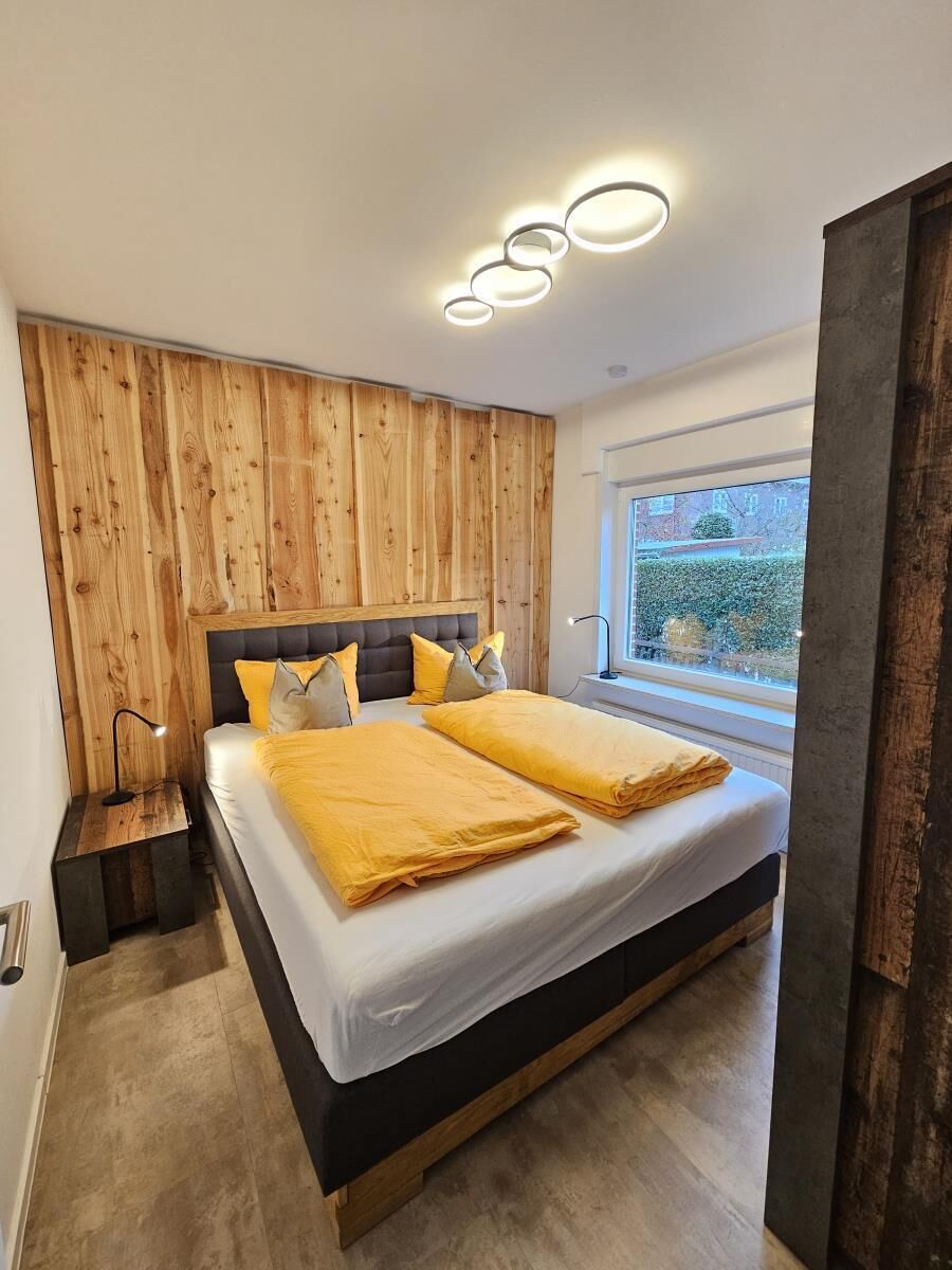 Une chambre moderne avec un mur d’accent en bois, un grand lit avec une literie jaune et une fenêtre donnant sur un paysage verdoyant.