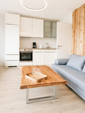 A modern kitchen with white cabinets, a wooden wall, and a grey sofa. - Apartment 5 in the Flechtner Building (Norderney)