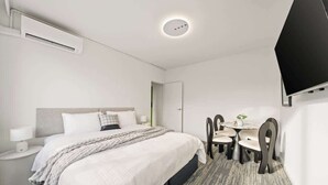 Ein Hotelzimmer mit Bett, Nachttisch, Lampe und einem Essbereich mit Stühlen und Tisch.