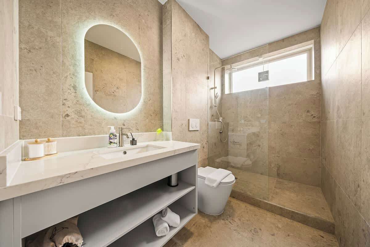 Une salle de bain moderne avec un meuble-lavabo en marbre, un grand miroir, une douche à parois de verre et des toilettes.