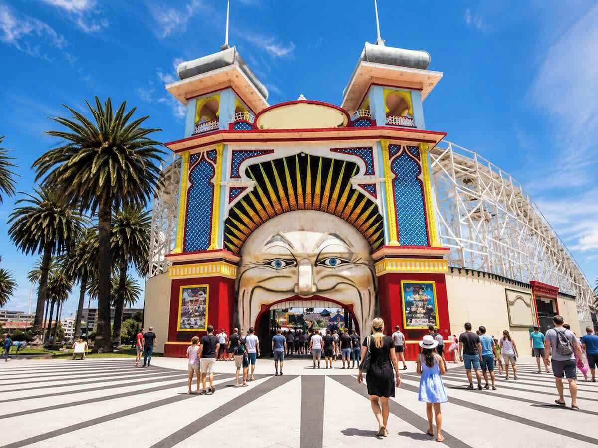 A large, colorful entrance with a prominent archway and a roller coaster in the background.