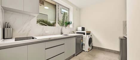 A compact kitchen with a built-in dishwasher, a microwave, and a window with blinds.