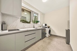 Eine kompakte Küche mit eingebautem Geschirrspüler, einer Mikrowelle und einem Fenster mit Jalousien.