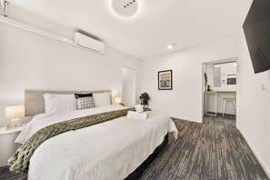 A hotel room with a bed, bedside table, lamp, air conditioning unit, and a television on the wall. - Family Suite with Two King Beds & St Kilda Charm (St Kilda)