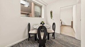 Et spiseområde med et rundt bord, fire stole, et vindue med persienner og en dør til et andet rum.