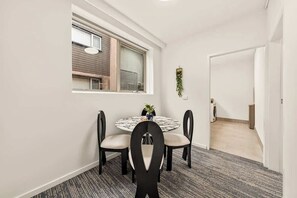 Ein Essbereich mit einem runden Tisch, vier Stühlen, einem Fenster mit Jalousien und einer Tür zu einem anderen Raum.