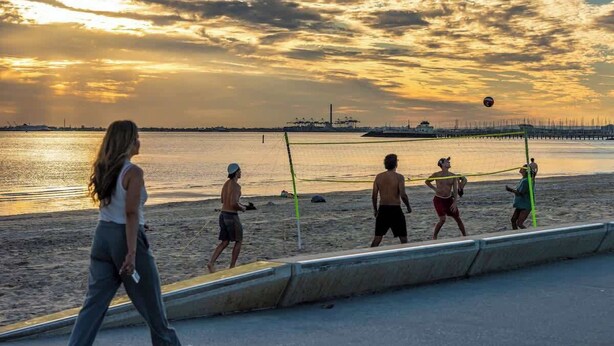 Volleyballspil på stranden med solnedgang i baggrunden.