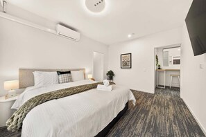 Une chambre d’hôtel équipée d’un lit, d’une table de chevet, d’une lampe, d’un climatiseur et offrant une vue sur la chambre voisine.