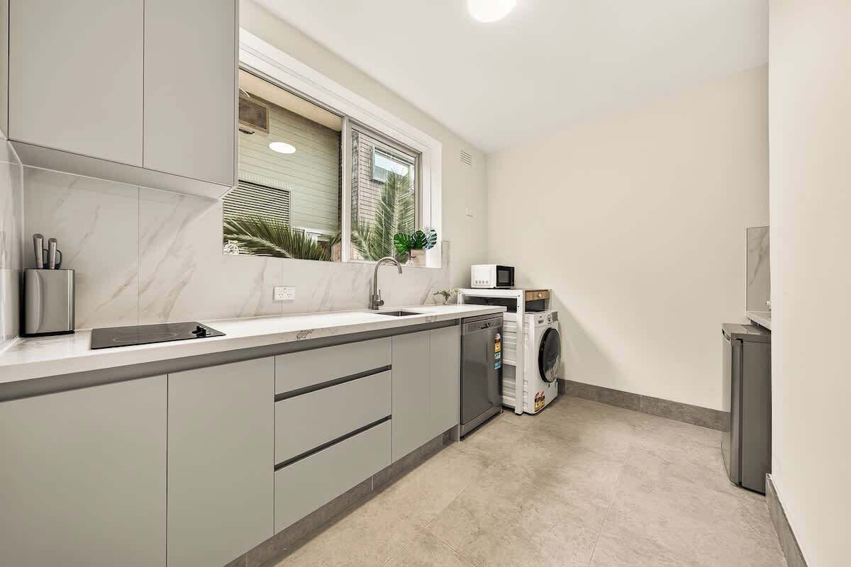 A compact kitchen with a built-in dishwasher, a microwave, and a window with blinds.