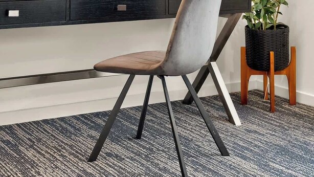 Ein moderner Arbeitsraum mit Schreibtisch, Stuhl, gerahmten Bildern, Regalen mit Büchern und Pflanzen sowie einem Blumentopf.