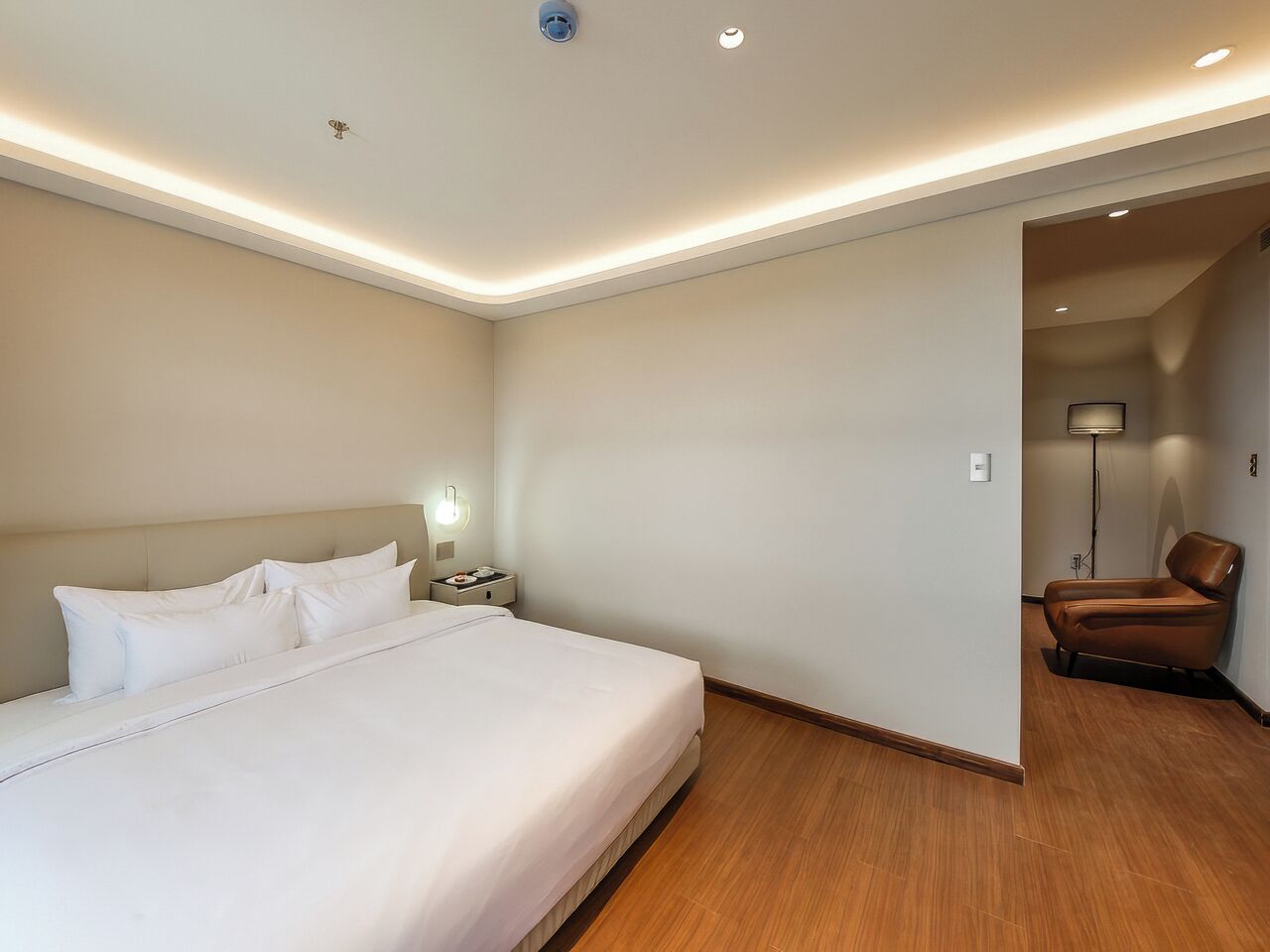 Habitación de hotel con cama, mesita de noche, lámpara y una silla.