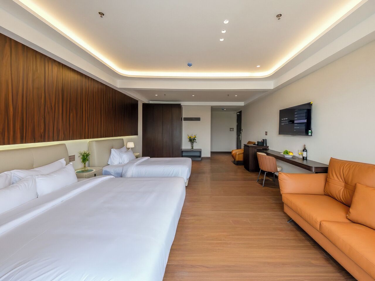A hotel room with two beds, a sofa, a desk, and a television.