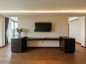 A modern room with a flat-screen TV mounted on the wall, a dark wooden desk with a vase of flowers, and a large window with curtains. - Pinewood Dalat (Lam Vien - Da Lat)