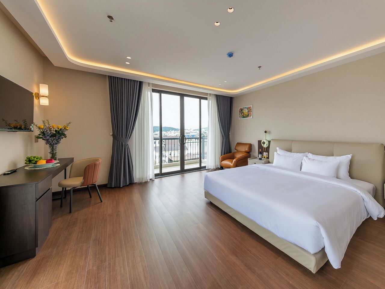 Ein Hotelzimmer mit einem großen Bett, einem Schreibtisch, einem Sessel und Blick auf die Stadt durch das Fenster.