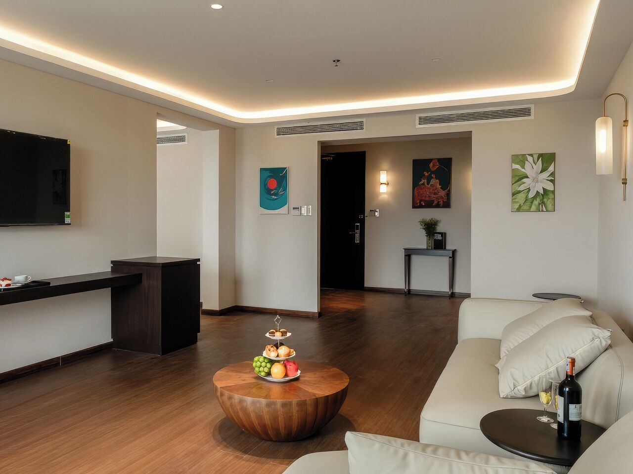 Ein modernes Wohnzimmer mit Couch, Fernseher an der Wand und Kunstwerken. Ein Holztisch steht im Raum.