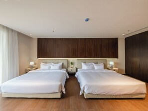 A hotel room with two beds, wooden flooring, a large wardrobe, and a nightstand with a lamp. - Pinewood Dalat (Lam Vien - Da Lat)