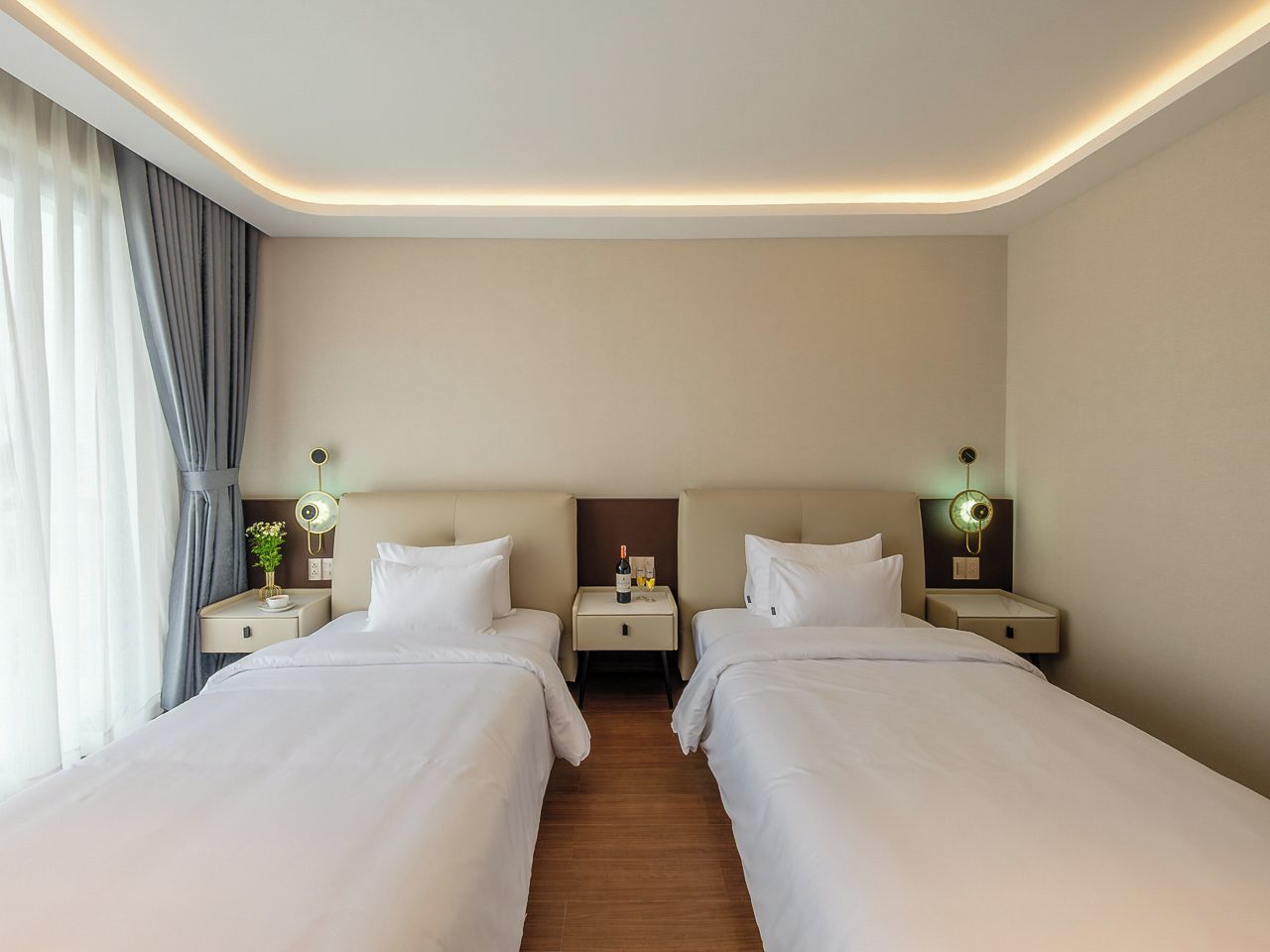 A hotel room with two beds, bedside tables, lamps, and a curtain.
