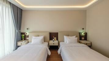 A hotel room with two beds, bedside tables, lamps, and a curtain.