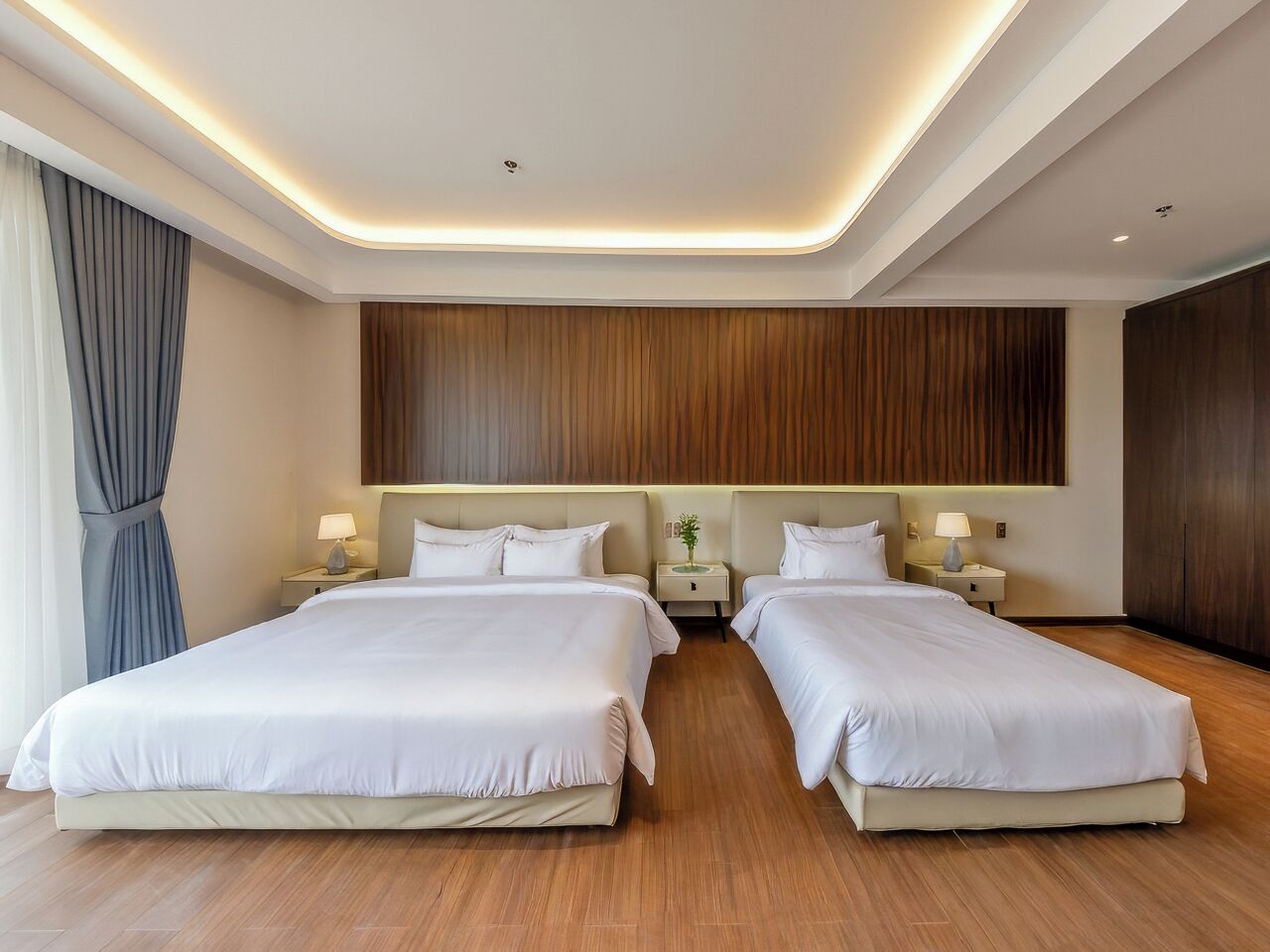 Ein Hotelzimmer mit zwei Betten, Holzboden und modernem Deckenstil.