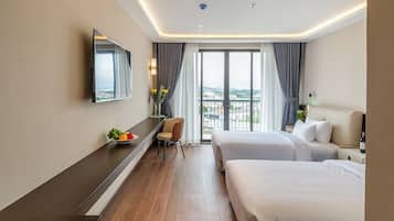 A hotel room with a large bed, a desk, a chair, a TV, and a balcony with a view.