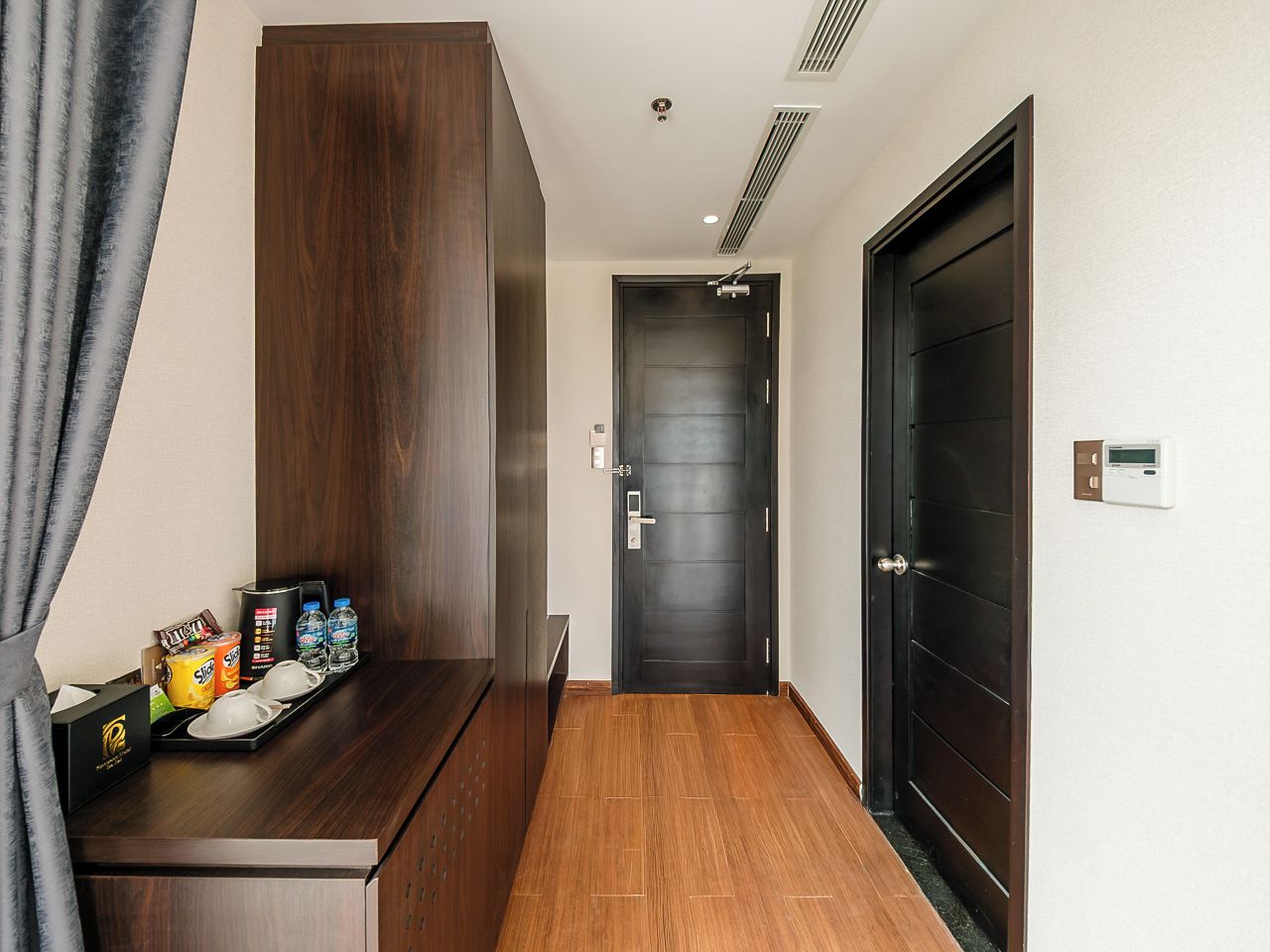 A hotel room with a wooden desk, a dark door, and a wall-mounted thermostat.