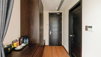A hotel room with a wooden desk, a dark door, and a wall-mounted thermostat.