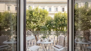 En balkon med et bord og stole, en potteplante og udsigt til en klassisk bygning.