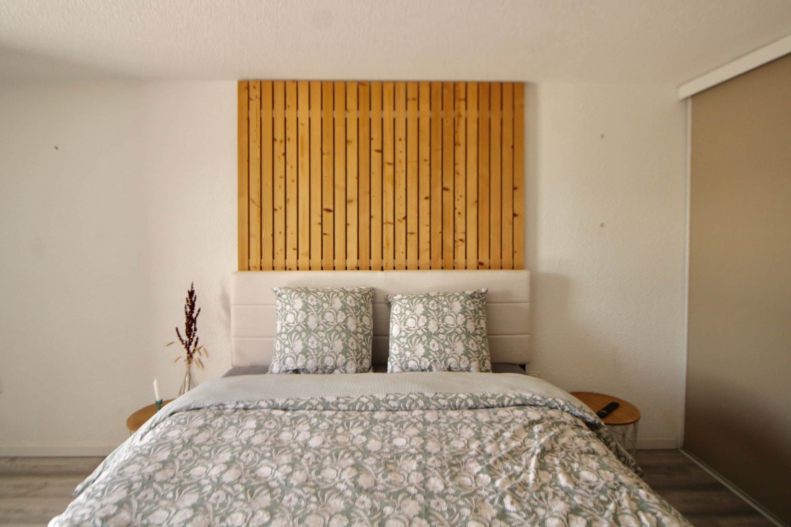 A bedroom with a bed, two pillows, a bedside table, and a wall-mounted headboard.
